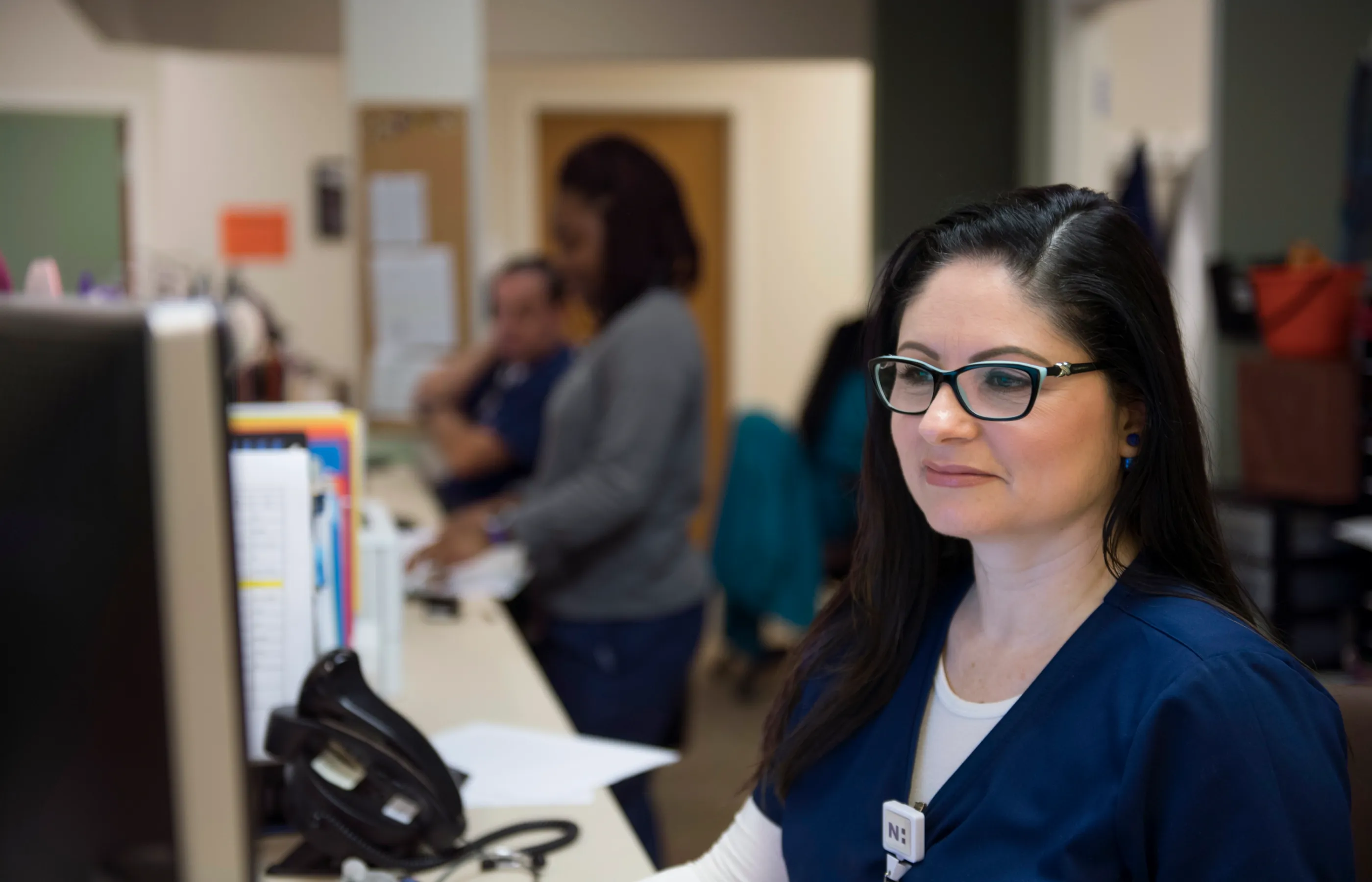 A Novant Health nurse is sitting at nurses station on a computer. 